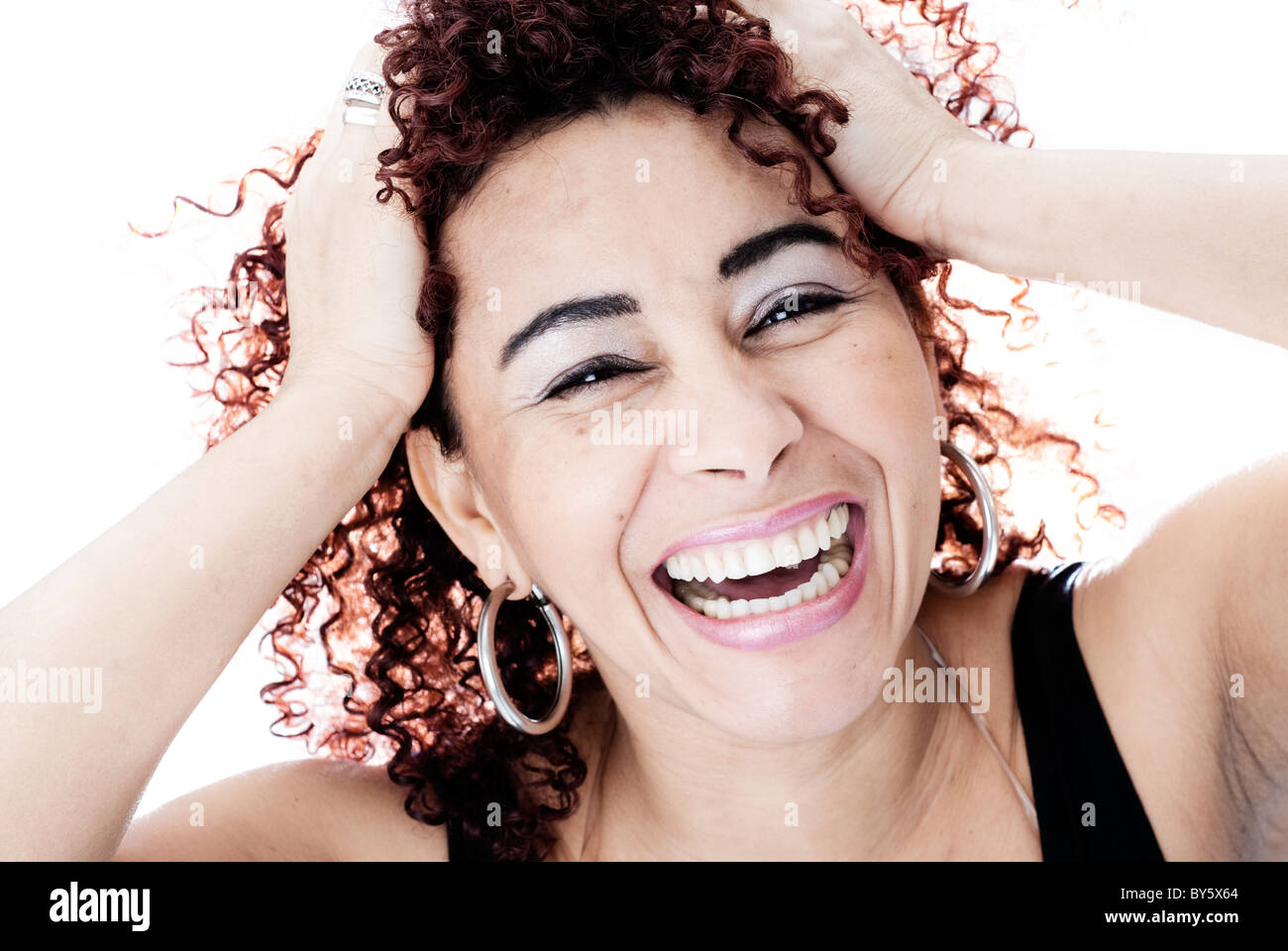 Brazilian woman smiling avec ses mains sur sa tête, a les cheveux bouclés et portait un débardeur noir Banque D'Images