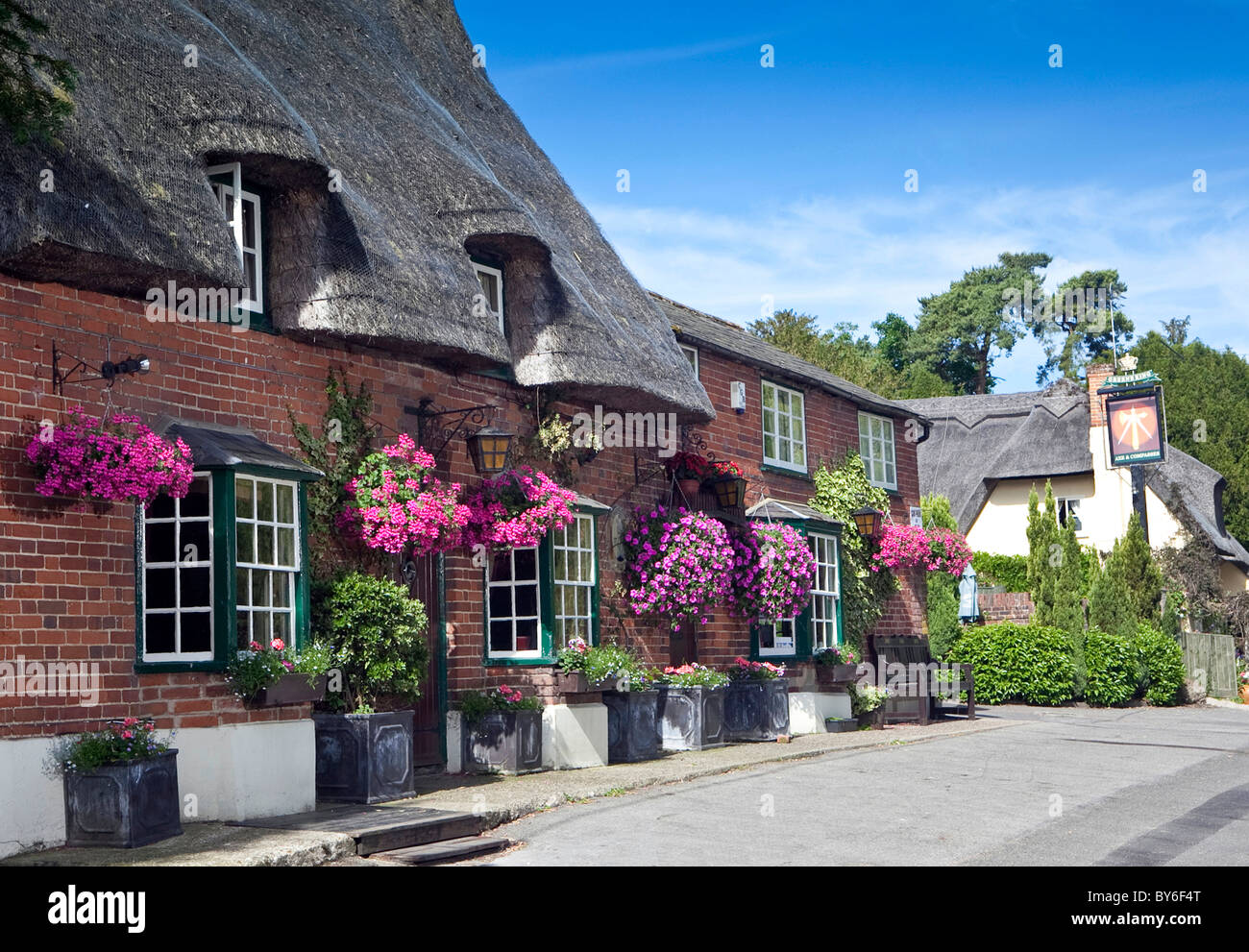 Le pub anglais traditionnel Ax et boussoles avec toit de chaume et des paniers de fleurs dans le village anglais de Arkesden, Essex Banque D'Images