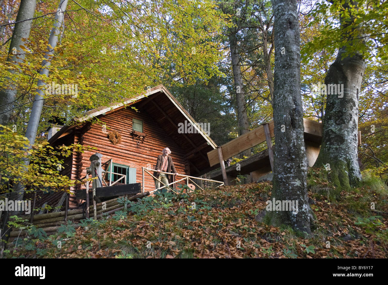 Homme plus âgé en face d'un chalet de montagne dans une forêt de feuillus, la Haute-Bavière, Allemagne Banque D'Images Homme plus âgé en face d'un chalet de montagne dans une forêt de feuillus, la Haute-Bavière, Allemagne Banque D'Images