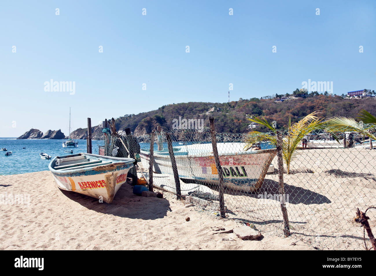 Plage de sable avec des bateaux de pêche colorés altérées échoués sur la clôture en fil de poulet & vista de Blue Bay à Puerto Angel Mexique Banque D'Images