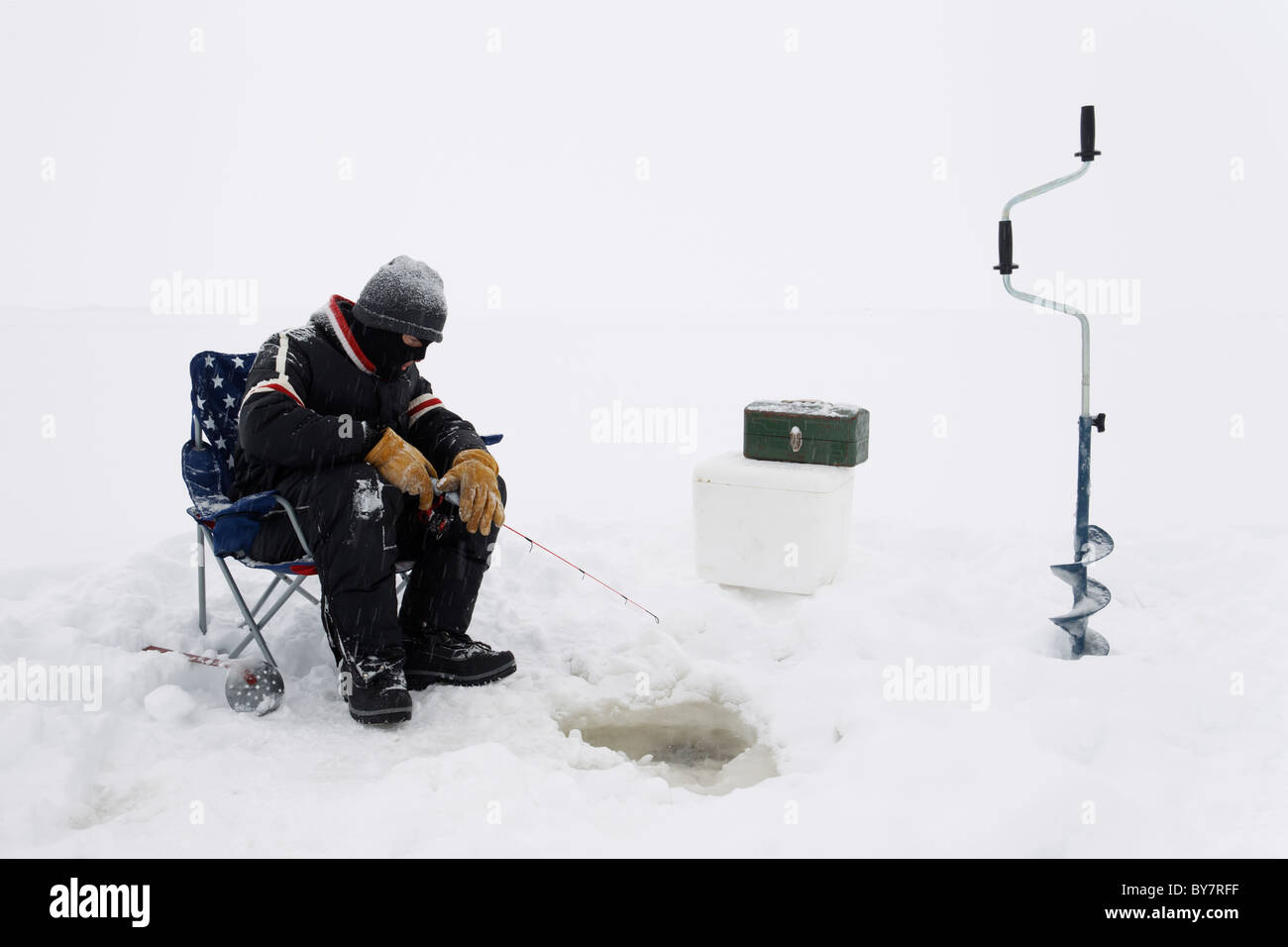 Un pêcheur sur glace attendent les poissons dans de la neige légère. Banque D'Images