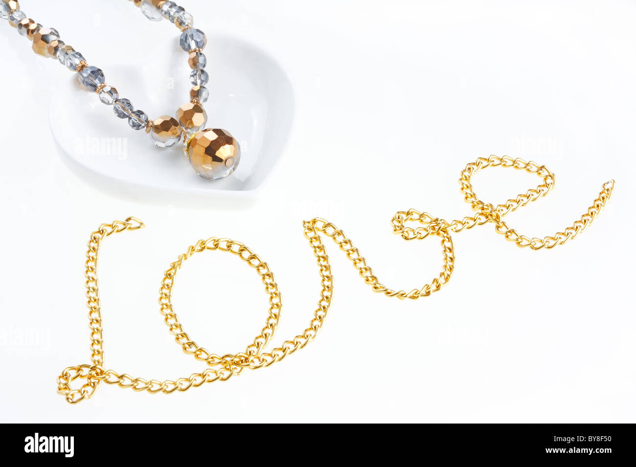 Collier bijoux en forme de coeur sur une soucoupe et chaîne en métal jaune disposés en forme de mot amour Banque D'Images