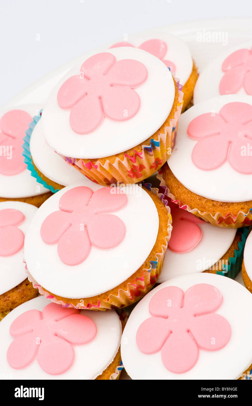 Gros plan d'une pile de petits cupcakes, également connus sous le nom de petits pains, avec glaçage blanc décoré de fleurs fondantes roses. Banque D'Images