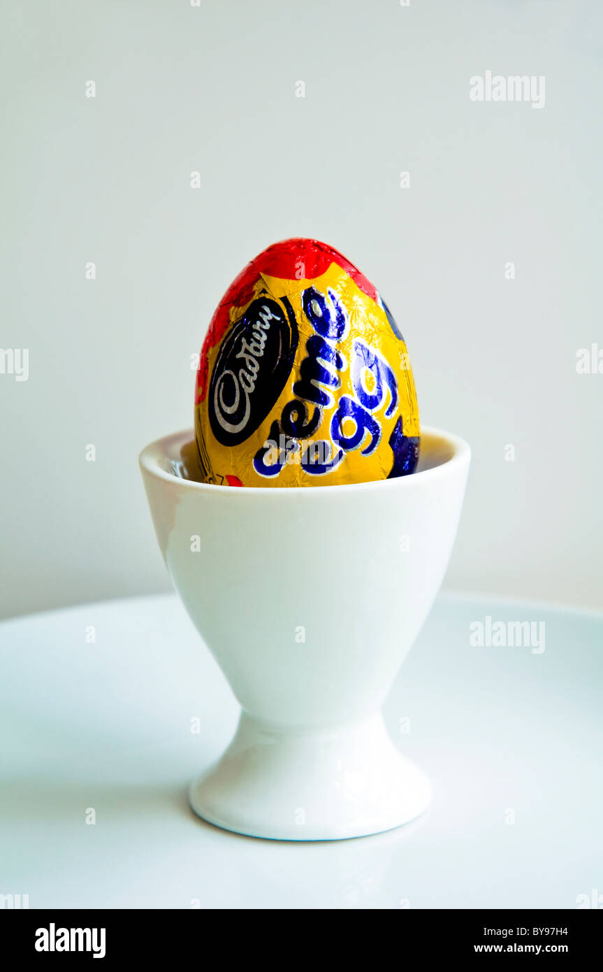 Un Cadbury Creme Egg in a white egg cup sur une plaque blanche. Banque D'Images
