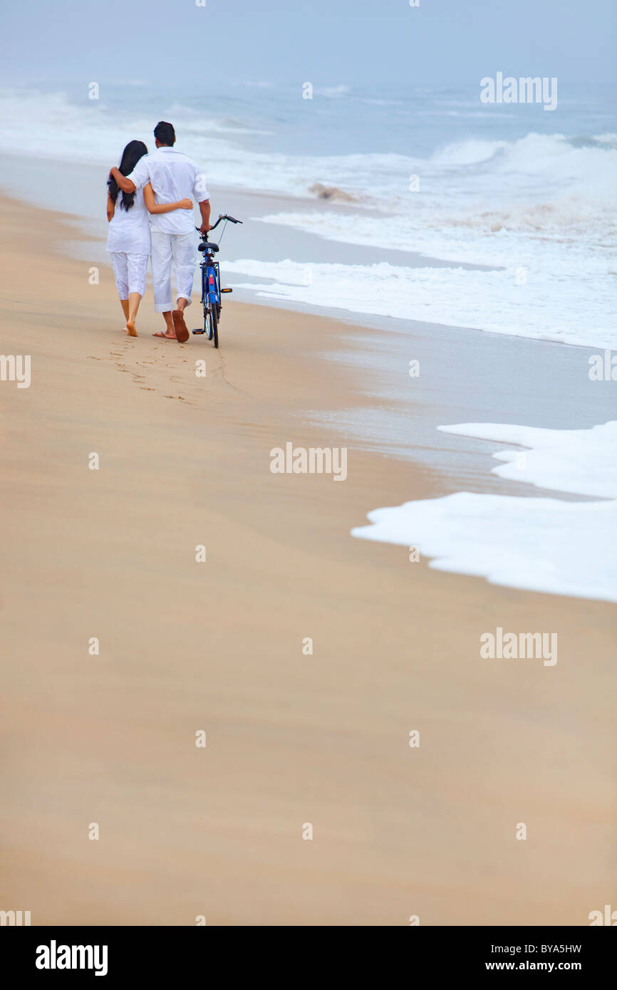Couple en train de marcher sur une plage avec un vélo Banque D'Images