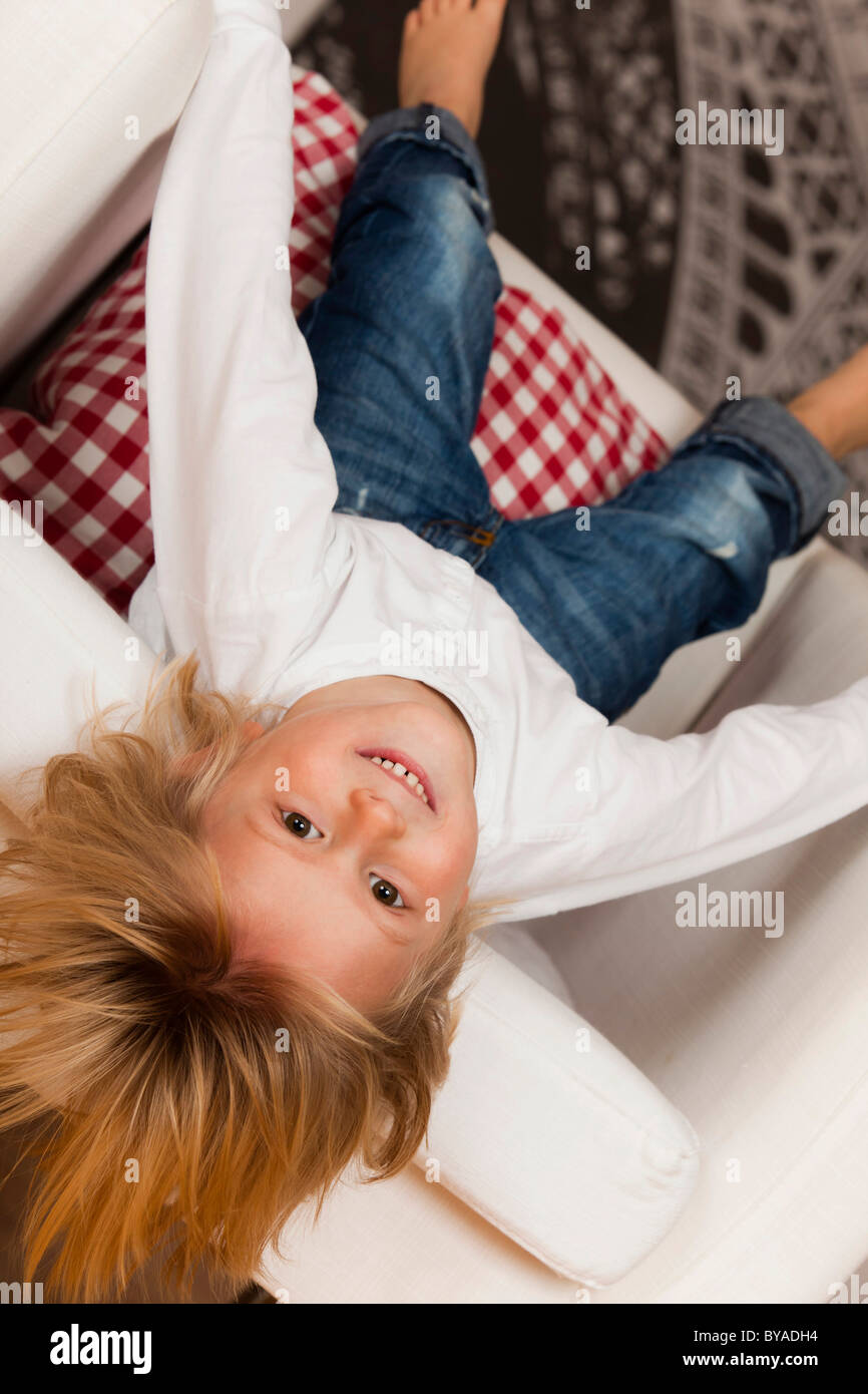 Garçon, 4 ans, tête en bas d'un fauteuil blanc Banque D'Images