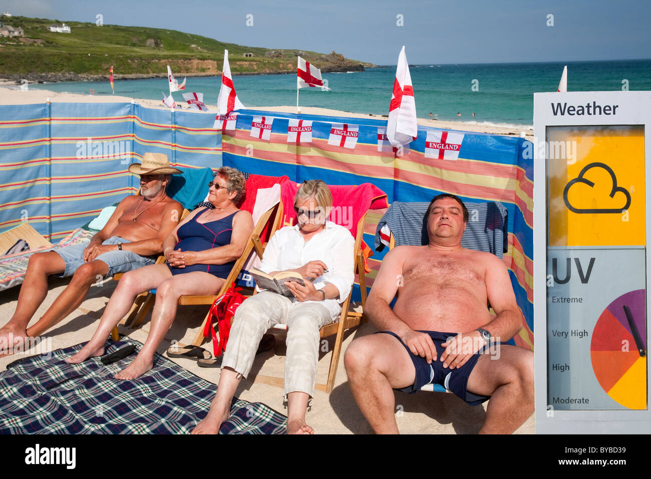 Les partisans de l'Angleterre de la coupe du monde à bronzer sur la plage à St Ives, Cornwall, UK, avec un panneau d'avertissement UV. Banque D'Images