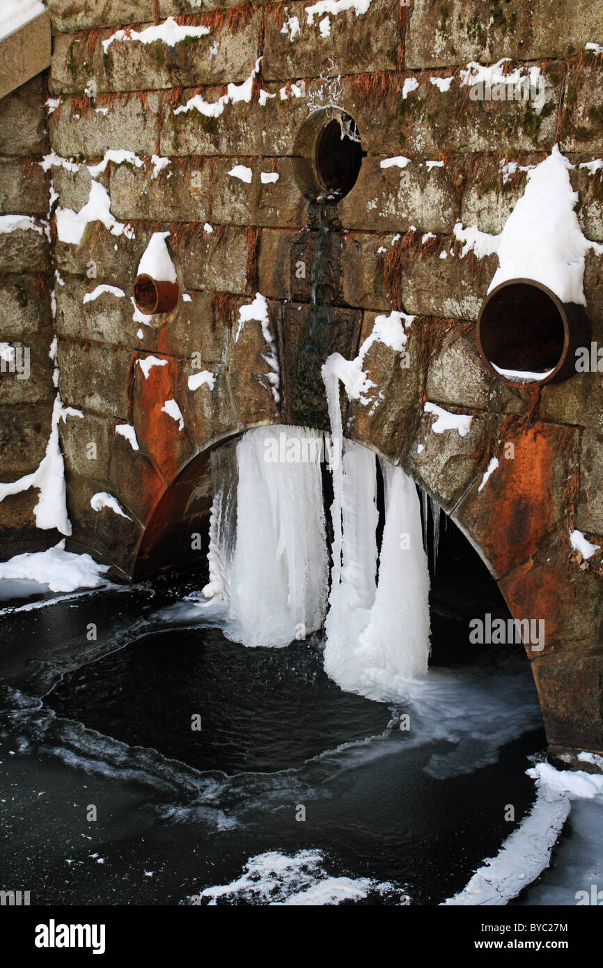 Un drain de l'eau de déversements vers le bas d'un mur de pierre et plus d'un aqueduc arch où il est gelé dans les glaçons Banque D'Images