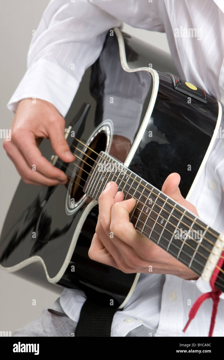 Un gros plan d'un homme de gratter une guitare acoustique noire. Banque D'Images