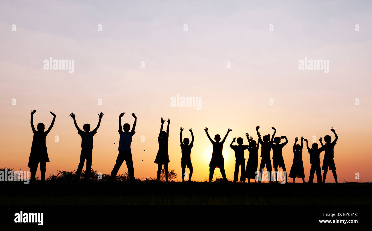 Filles et garçons indiens Silhouette sautant et brandissant debout sur un champ de riz au coucher du soleil. L'Andhra Pradesh, Inde Banque D'Images