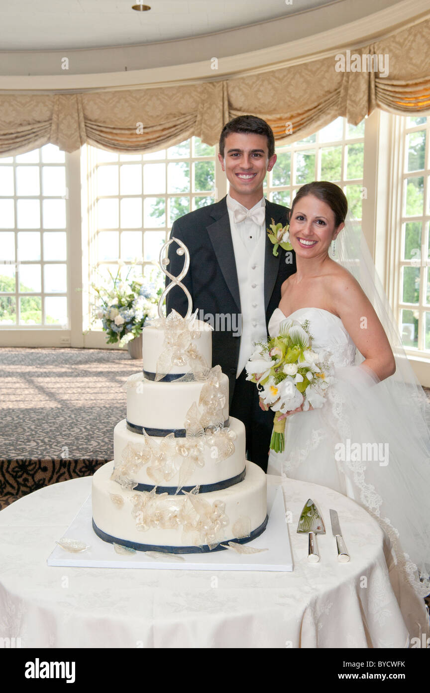 Belle mariée et le beau palefrenier devant leur gâteau de mariage. Banque D'Images