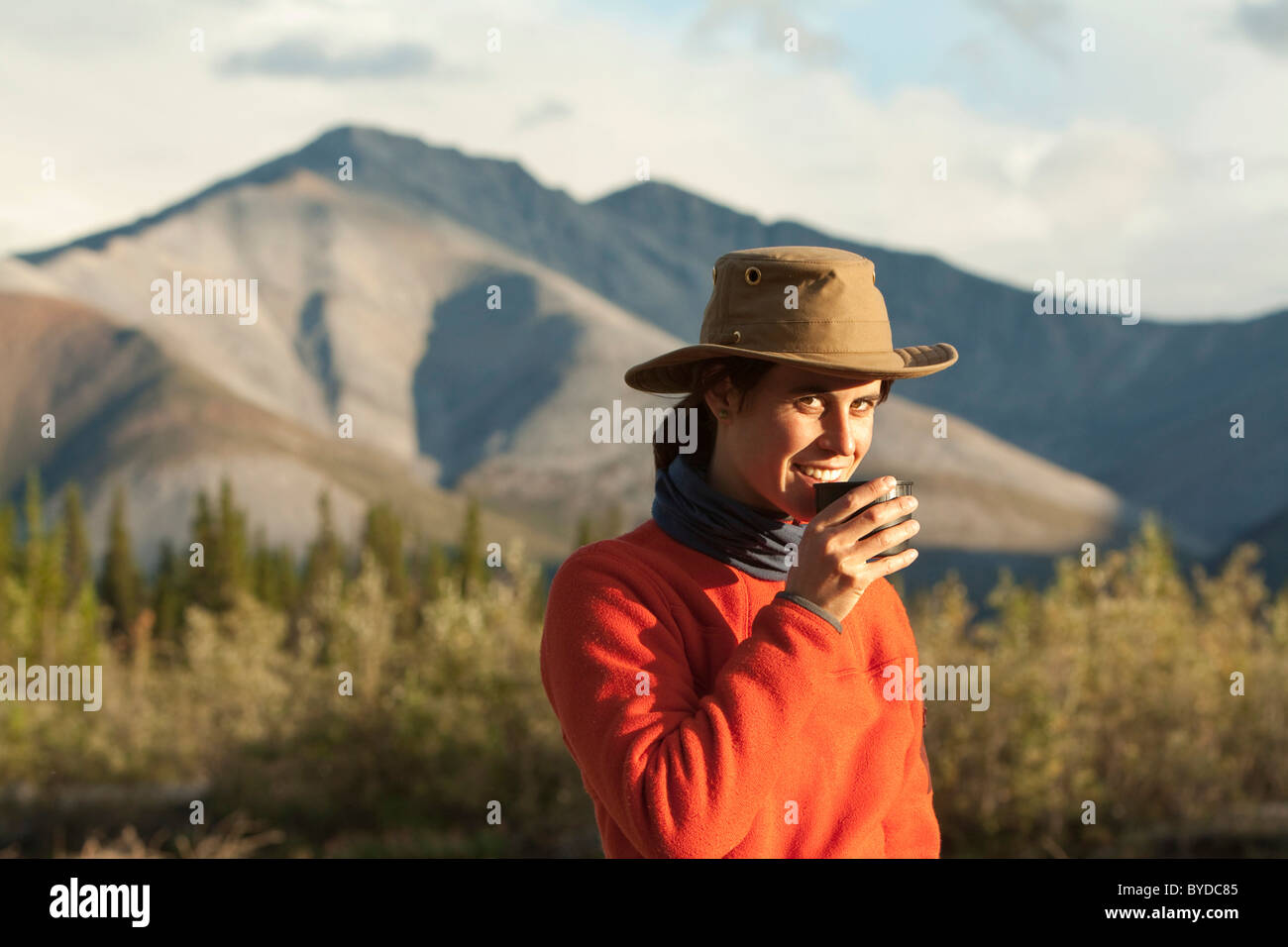 Jeune femme à boire, prendre une tasse de thé, Wind River, dans le nord des monts Mackenzie derrière, Territoire du Yukon, Canada Banque D'Images