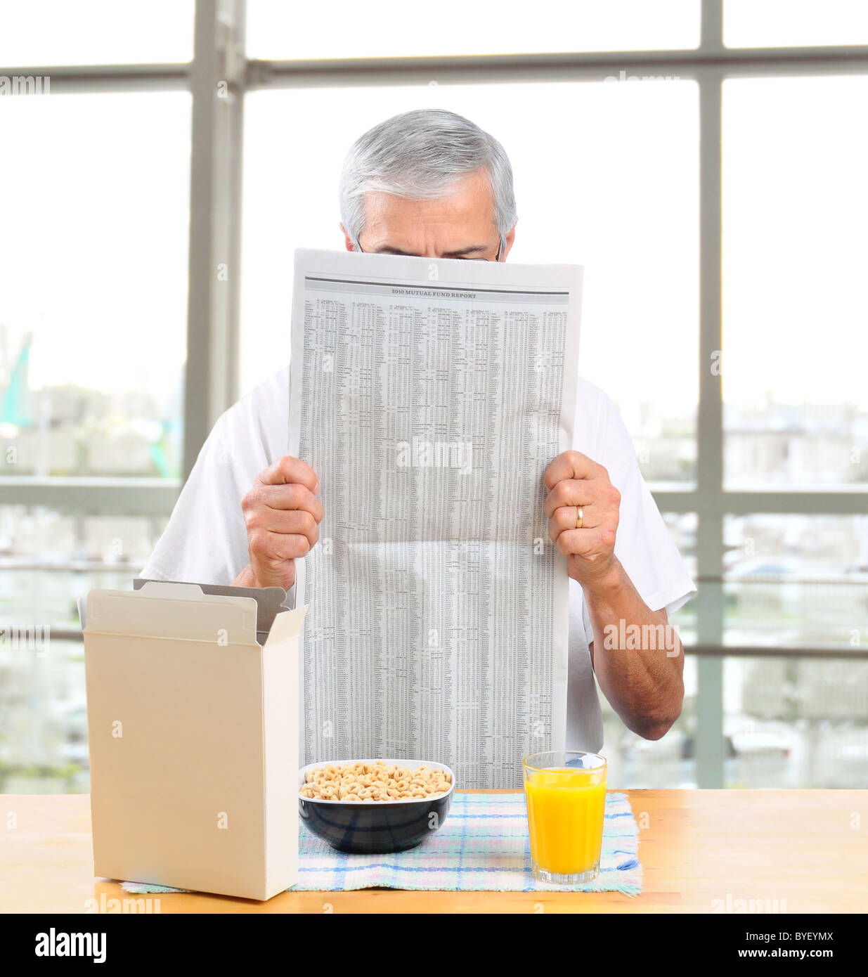 Homme d'âge moyen habillé en passant de la lecture du journal du matin en face de grande fenêtre avec céréales petit déjeuner en face de lui. Banque D'Images