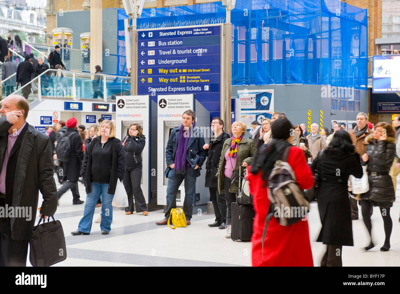 Les banlieusards de London Liverpool Street Station passagers foule chercher le départ des arrivées à bord en attente de la formation de certains sur la cellule ou téléphones mobiles Banque D'Images