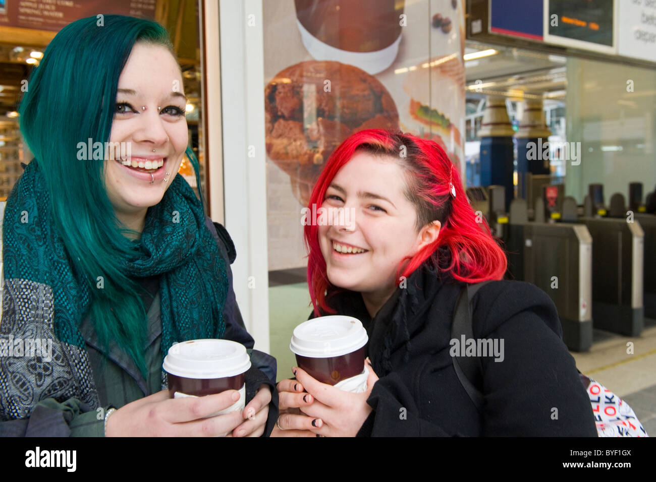 La gare de Liverpool Street Station deux jolies jeunes filles femmes mesdames vert & rouge à lèvres piercing nez cheveux bouche tasses à café smiling rire heureux Banque D'Images