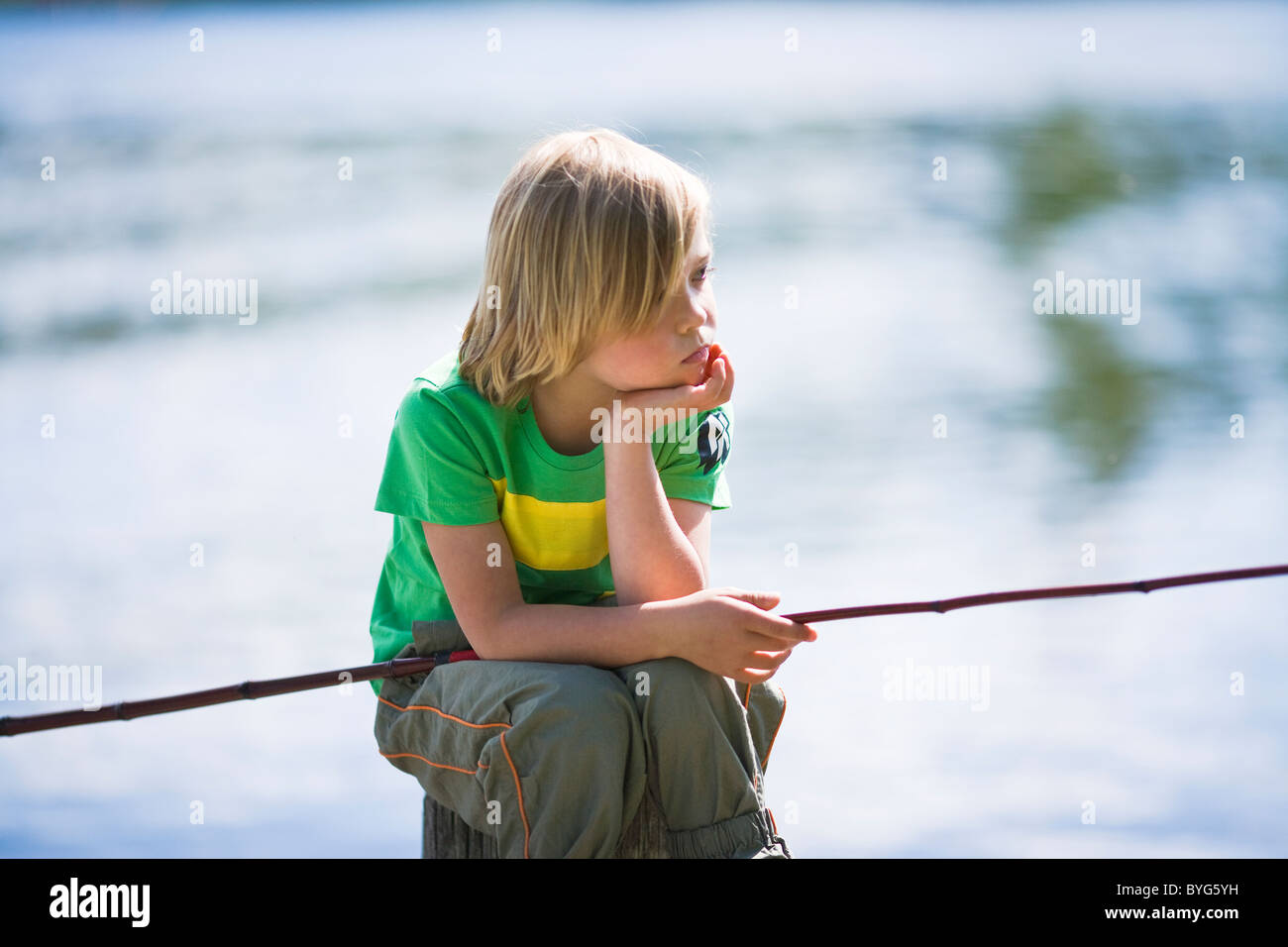 Bored boy sitting on jetty avec canne à pêche Banque D'Images