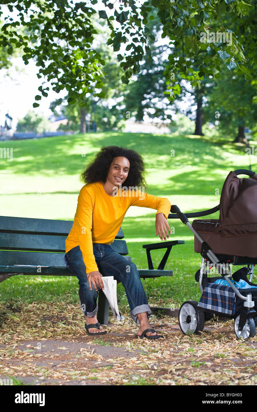 Smiling Young man with baby carriage sitting on bench Banque D'Images