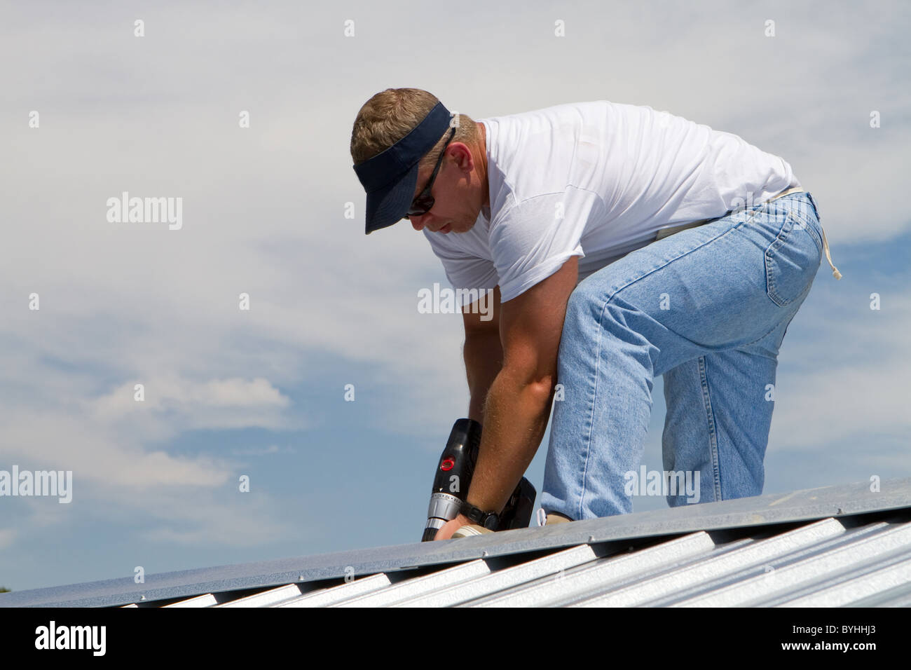 Travailleur de la construction utilise une perceuse pour fixer un plafond le haut d'une feuille de travail de toiture en métal à l'aide de vis. Banque D'Images