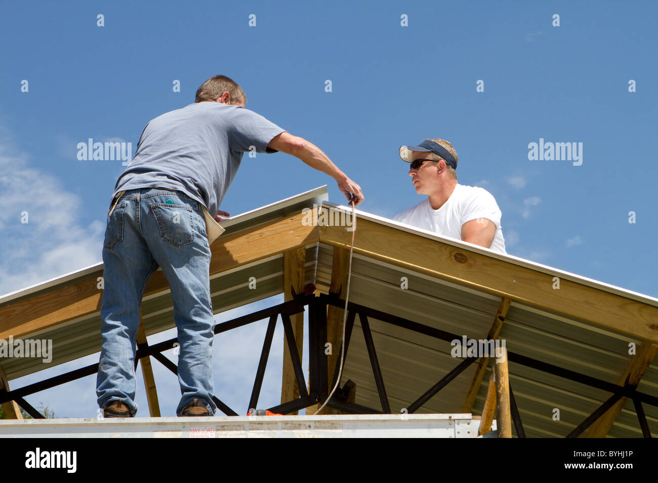 Les travailleurs de la construction de toitures en tôle s'appliquent à un toit de grange. Banque D'Images