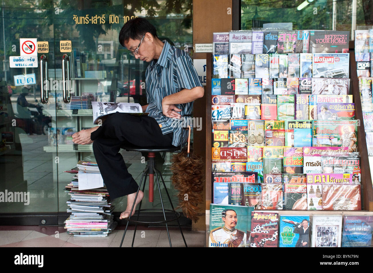 Vendeur de journaux la lecture d'un magazine à l'avant de la boutique, Bangkok, Thaïlande Banque D'Images