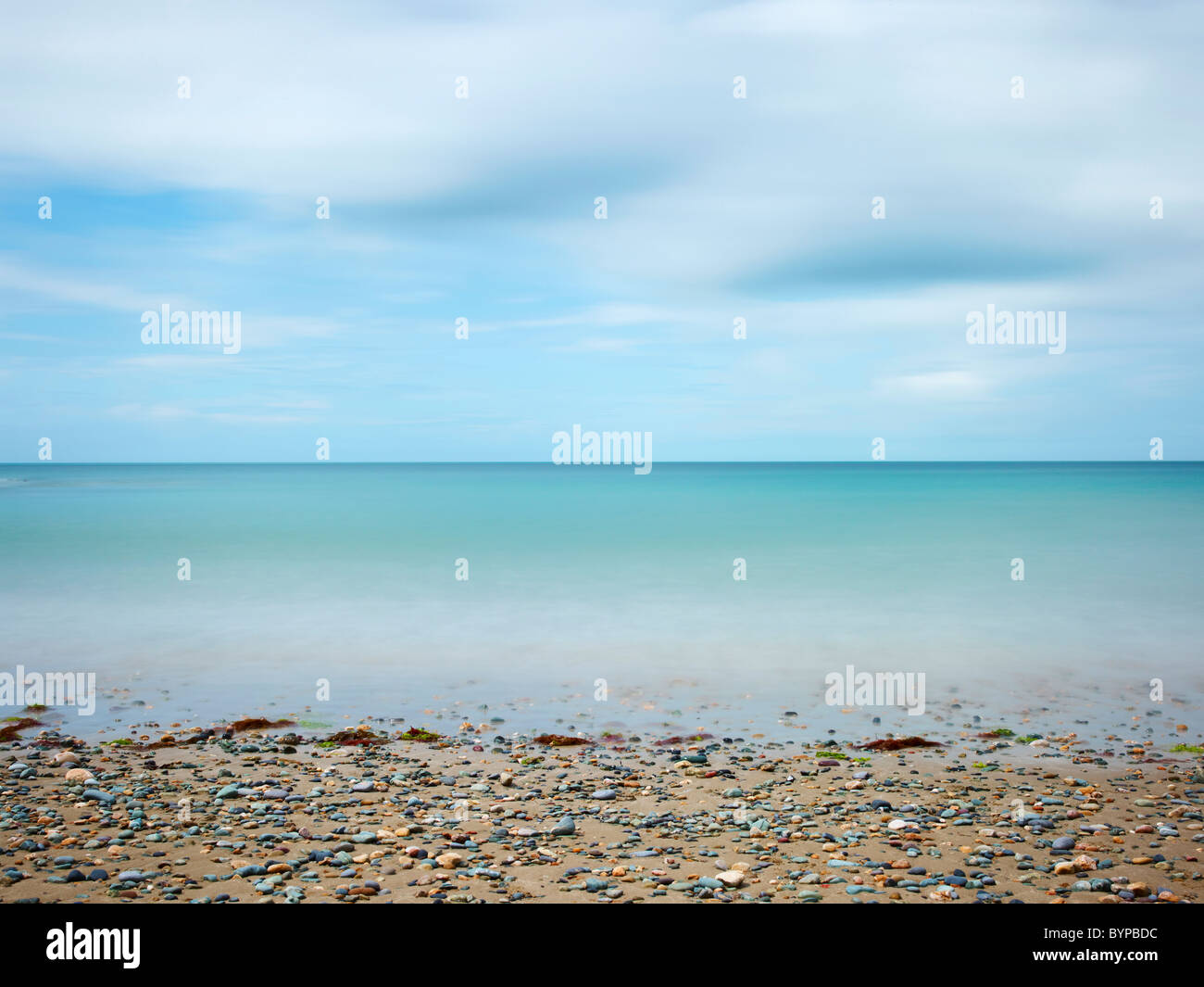 Photographie de paysage marin de la baie d'Anglesey au Pays de Galles, une longue exposition à la lumière du jour donnant mouvement dans le ciel et sur la mer avec plage de galets Banque D'Images