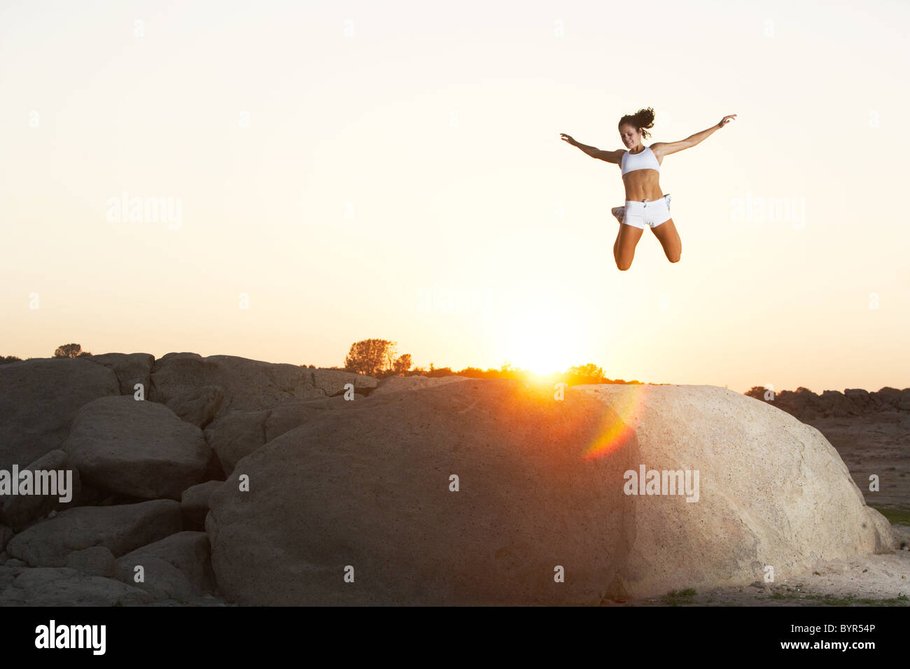 Une femme saute de joie sur à d'un rocher surplombant un lac Banque D'Images
