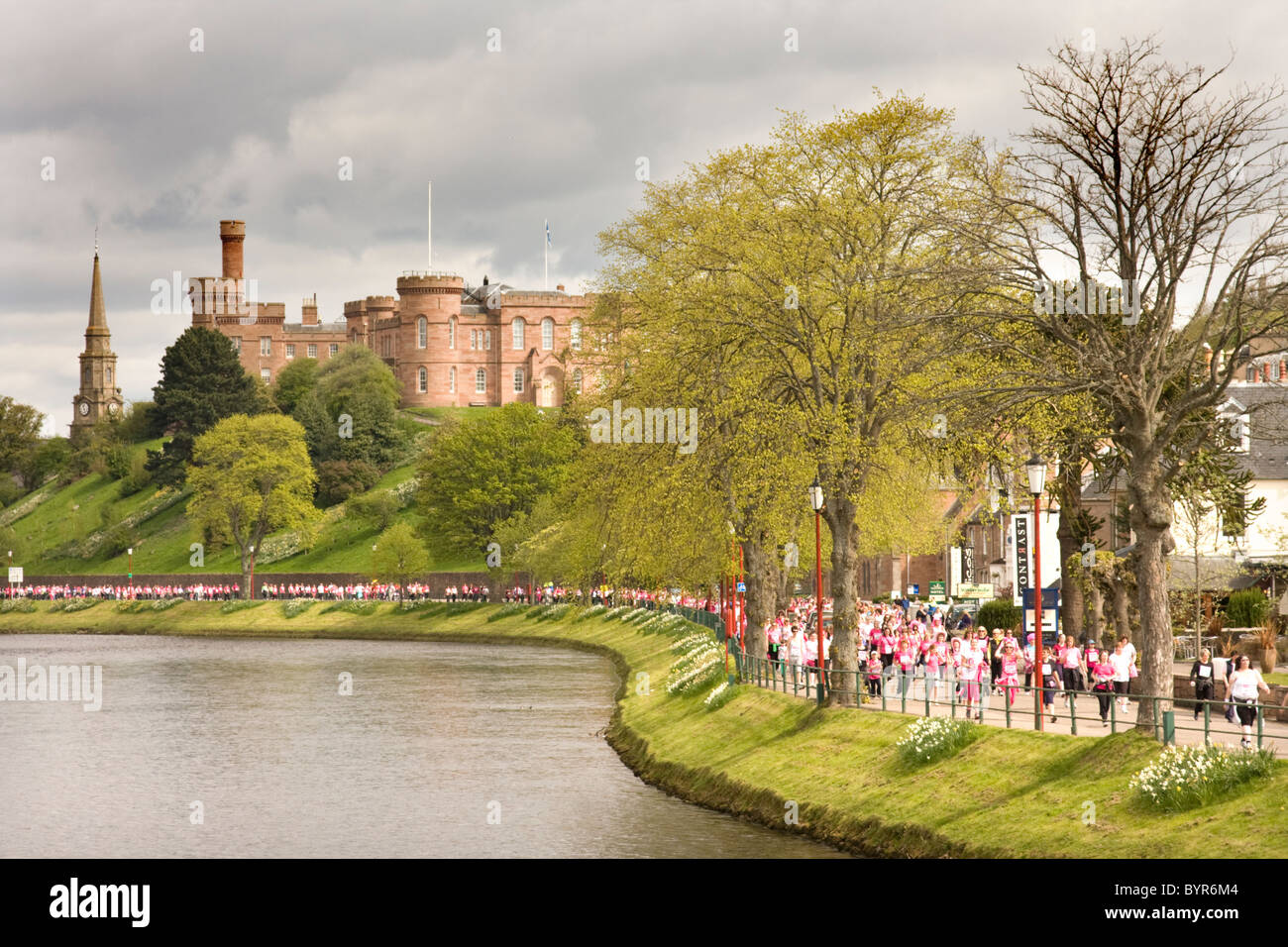 Le Château d'Inverness surplombant la rivière Ness, et la course pour la vie en rose en passant par les coureurs. Banque D'Images Le Château d'Inverness surplombant la rivière Ness, et la course pour la vie en rose en passant par les coureurs. Banque D'Images