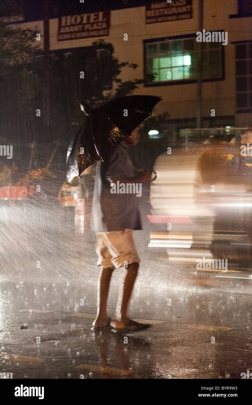 L'Inde, Agra, Uttar Pradesh avec parapluie homme échoué en milieu de route très fréquentée la nuit pendant la pluie de mousson Banque D'Images