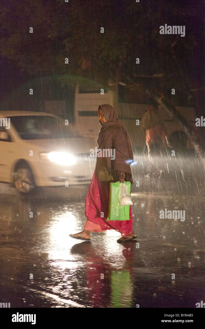 L'Inde, l'Uttar Pradesh, Agra dame crossing road dans de fortes pluies de mousson Banque D'Images