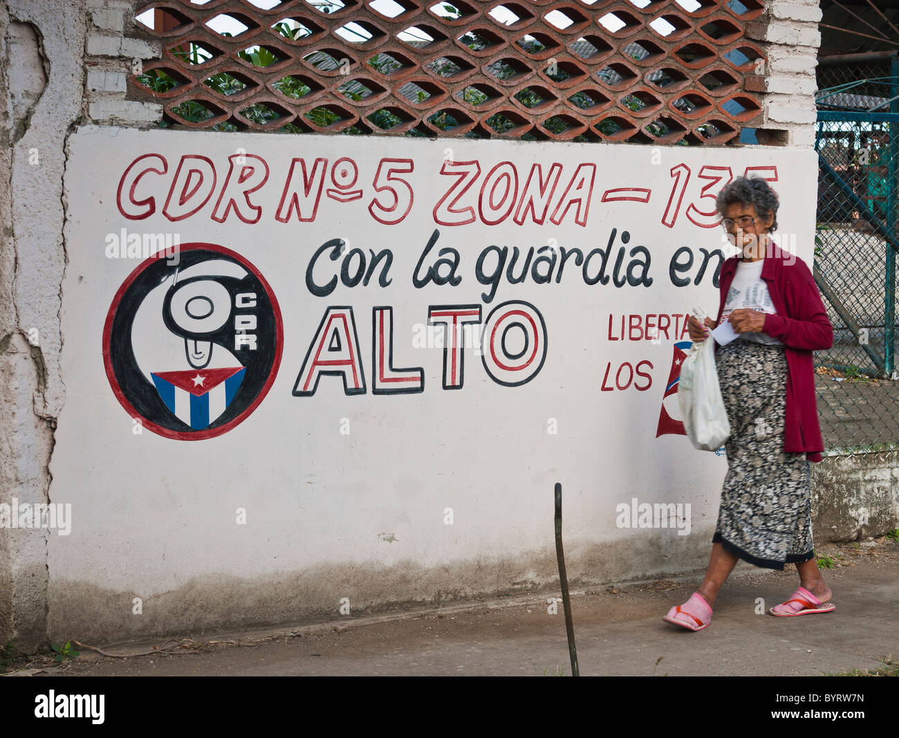 Femme marche par un graffiti d'un symbole politique Camaguey, Cuba, Caraïbes. Banque D'Images