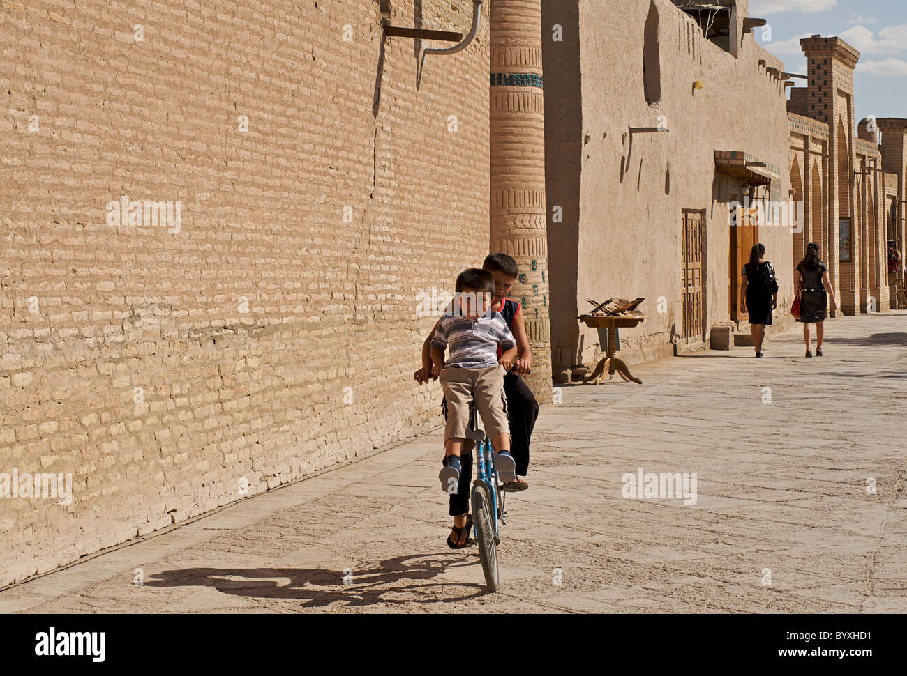 Enfants Uzbeki partager un vélo dans la rue. Ichon-Qala, Khiva, Ouzbékistan Banque D'Images