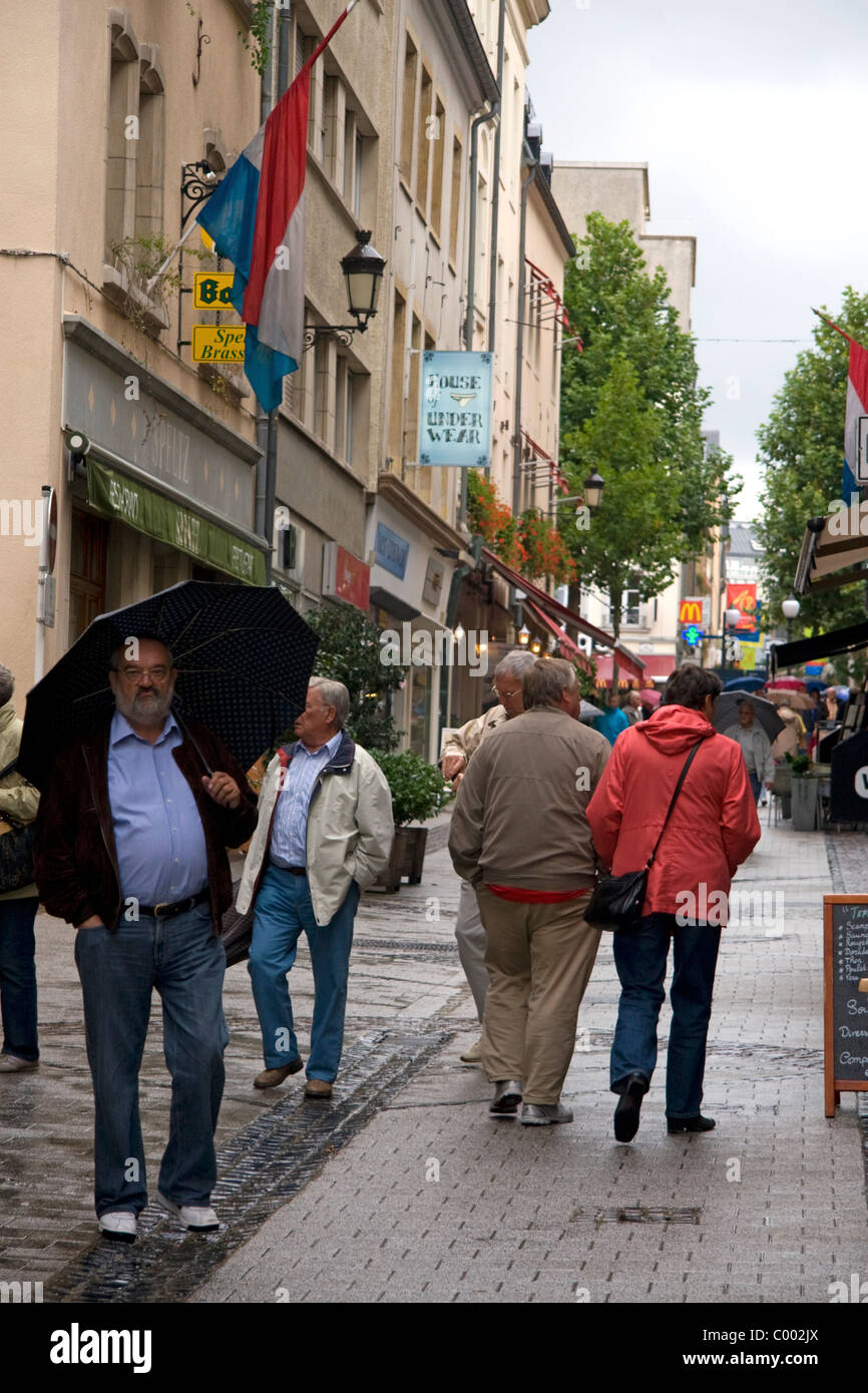 Les piétons marcher sous la pluie sur une rue piétonne dans la ville de Luxembourg, Luxembourg. Banque D'Images