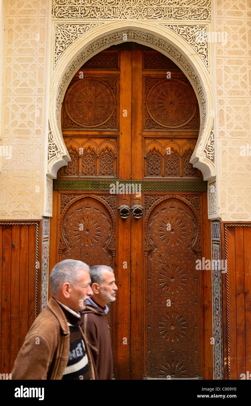 Deux hommes en brun en bois orné de marche par portes d'une mosquée de Médina de Fès Maroc Banque D'Images