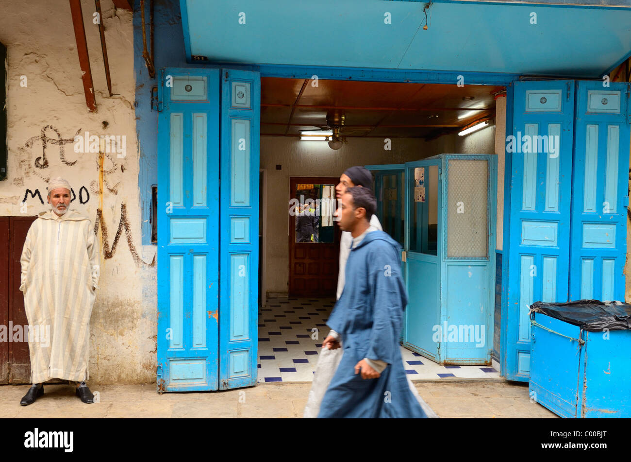 Homme marocain regarder les hommes marcher par en djellabas et caps en bleu Fes el Bali medina Fez Maroc Banque D'Images