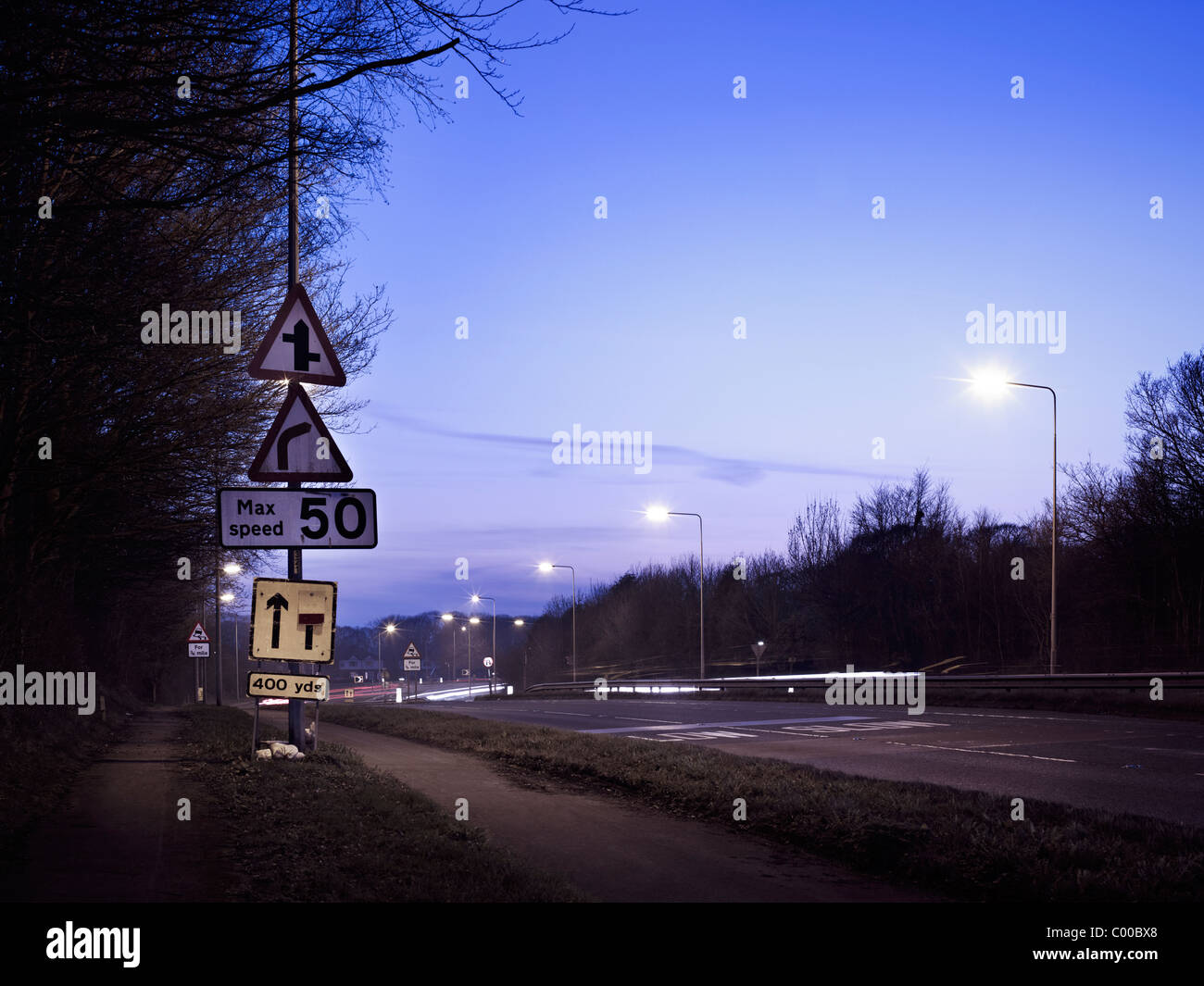 Route et arbres éclairés par des lumières de rue dans la nuit avec un ciel bleu , pris par endroits Banque D'Images
