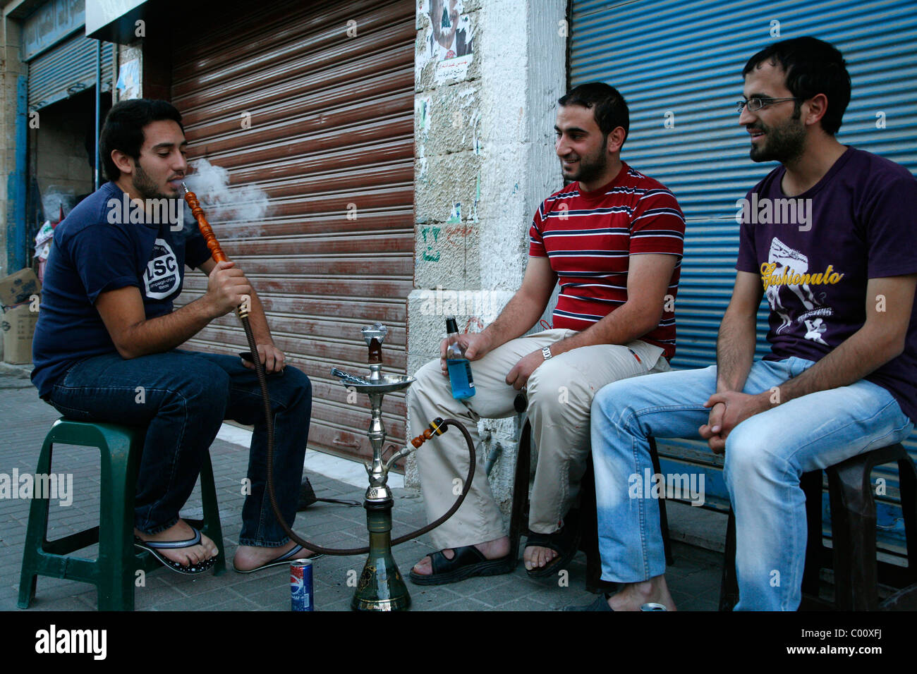 Les jeunes hommes fumeurs narguilé (pipe à eau) dans une rue de Madaba, Jordanie. Banque D'Images