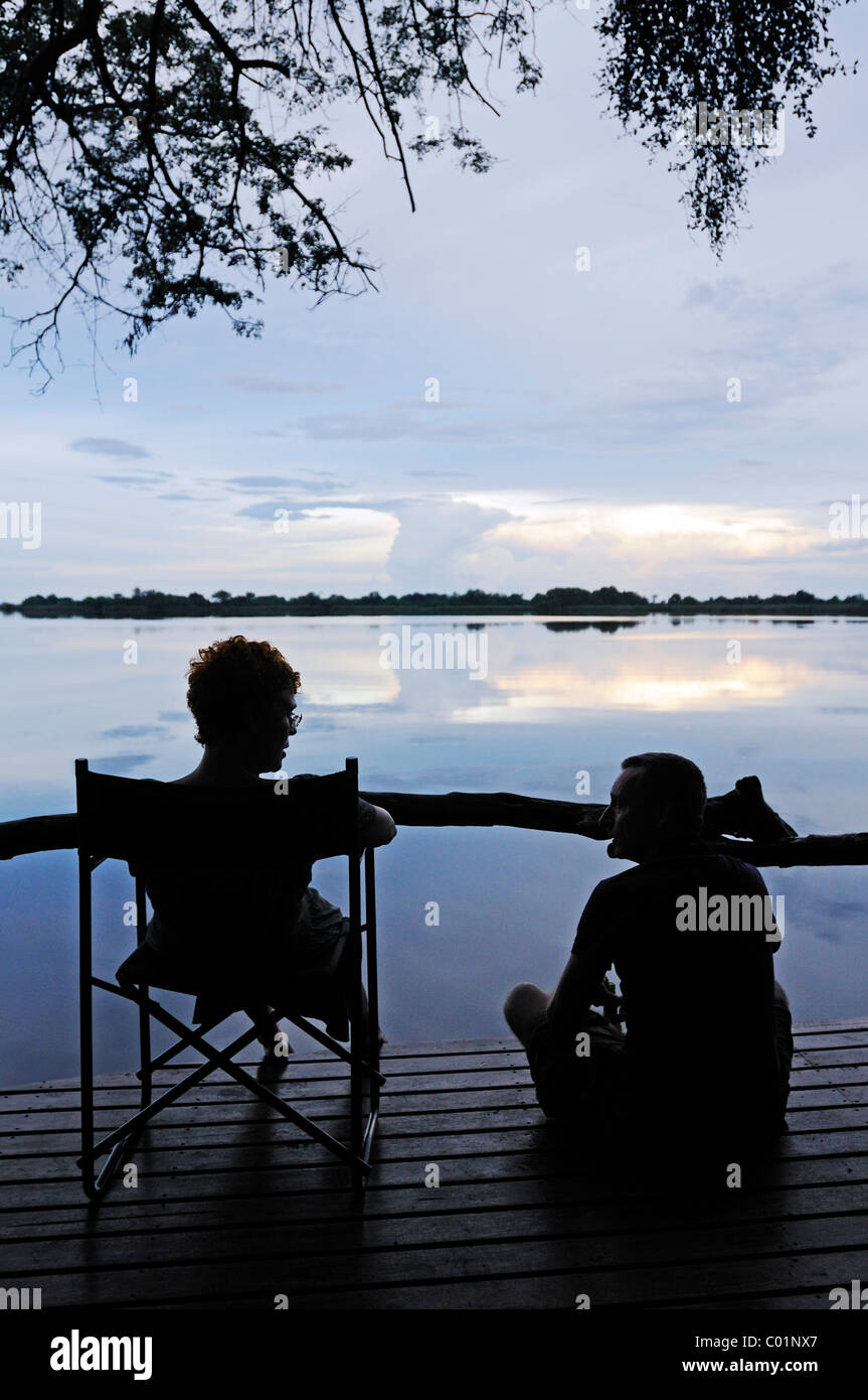 Les touristes assis sur la terrasse d'un lodge dans la soirée, Guma Guma Lagoon, lagune, Okavango Delta, Botswana, Africa Banque D'Images