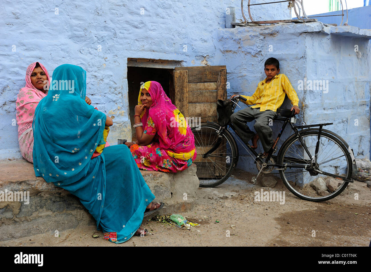 Trois femmes indiennes portant des saris colorés parle en dehors de leur maison, un garçon assis sur son vélo Banque D'Images