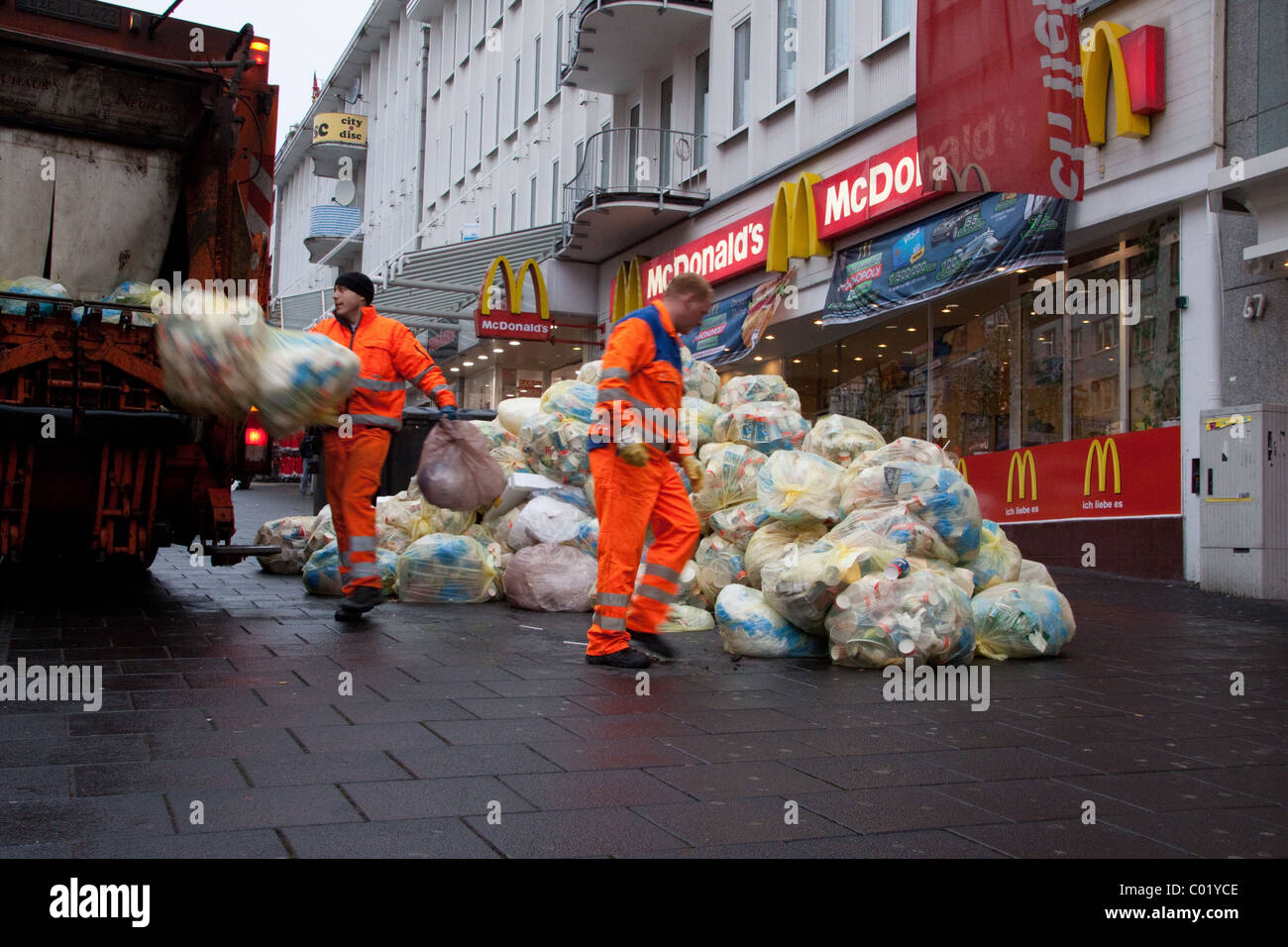 Des sacs de déchets d'emballage ont été empilés dans la rue Sont emmenés loin de l'extérieur d'un restaurant McDonald's de restauration rapide par collecteurs de déchets / bin hommes Banque D'Images