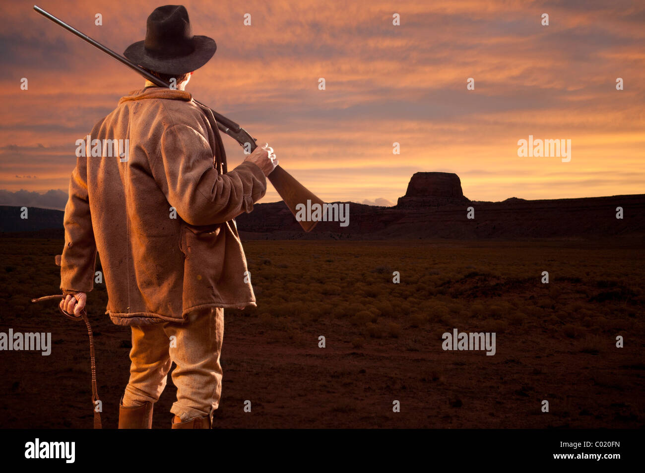 Cowboy holding gun est à la recherche au coucher du soleil à Monument Valley Utah. Banque D'Images