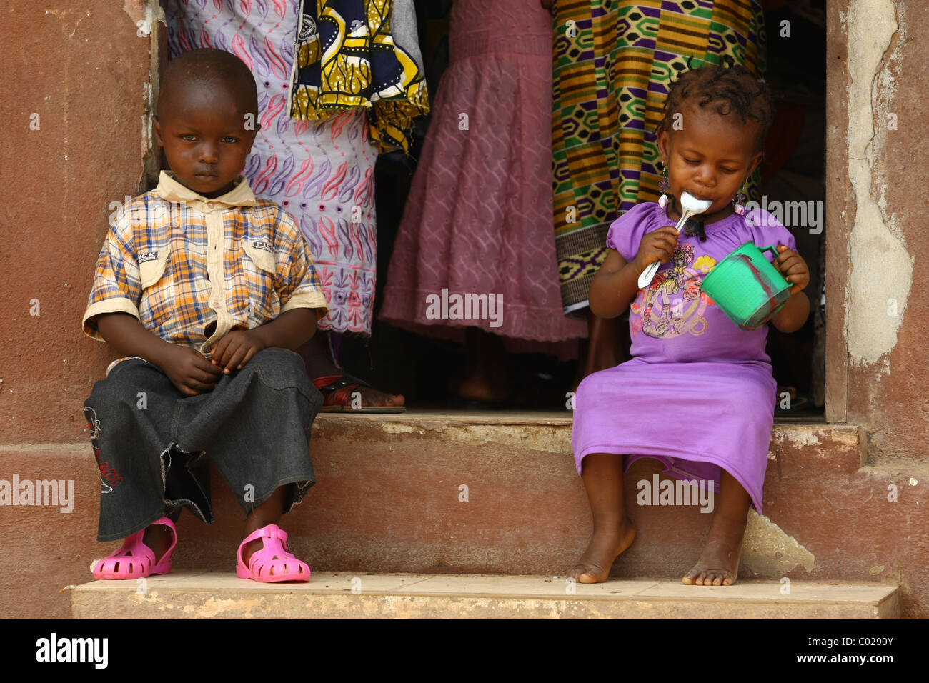 Une fille mange tout en étant assis à côté d'un garçon à l'extérieur de la communauté Binkolo centre de santé dans le village de Binkolo, Sierra Leone Banque D'Images