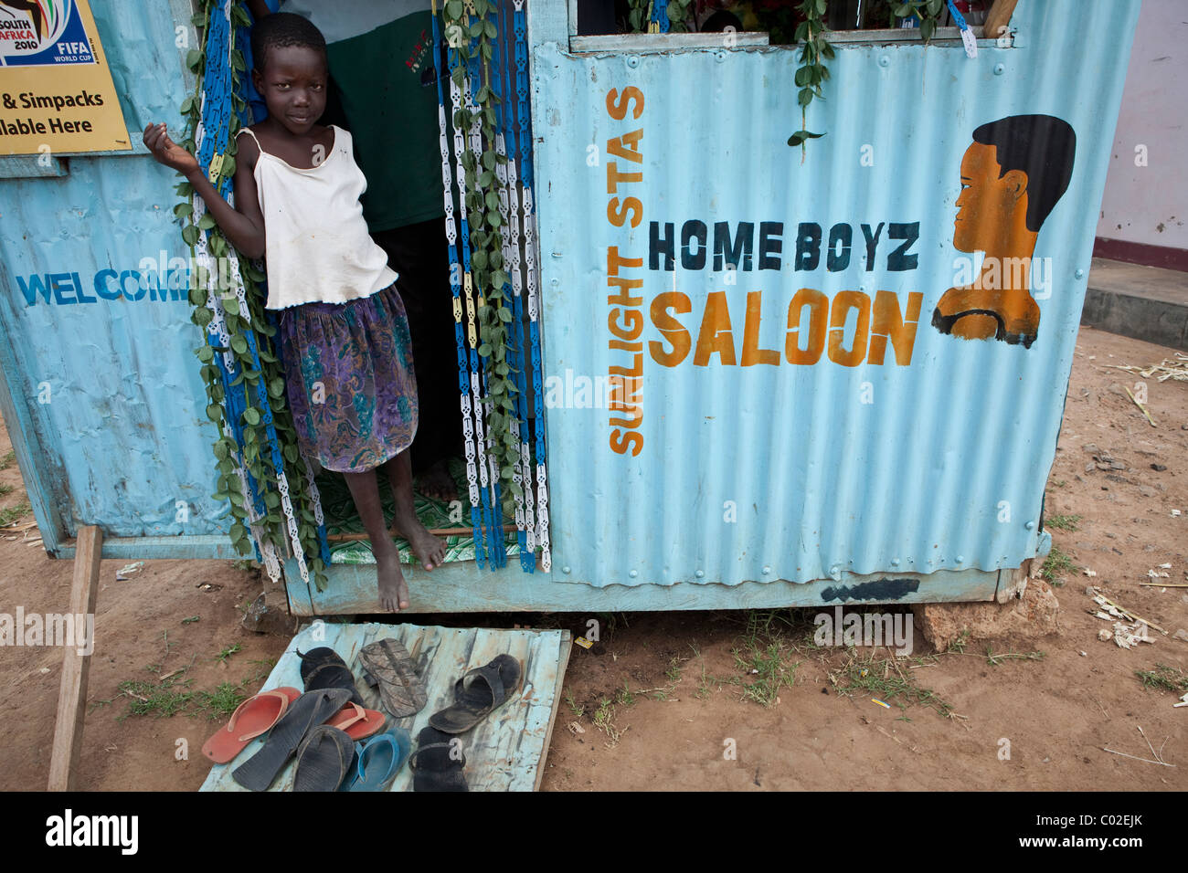Une jeune fille se tient en dehors d'une coupe de cheveux salon en Ouganda, Amuria, Afrique de l'Est. Banque D'Images