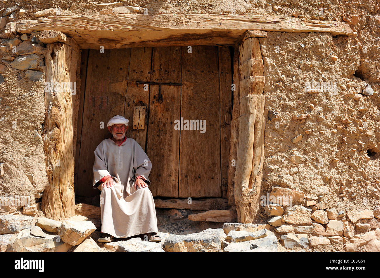 Personnes âgées Le Berbère homme portant un turban traditionnel Djellabah et assis à l'entrée d'un ancien silo de stockage, ait Bouguemez Banque D'Images