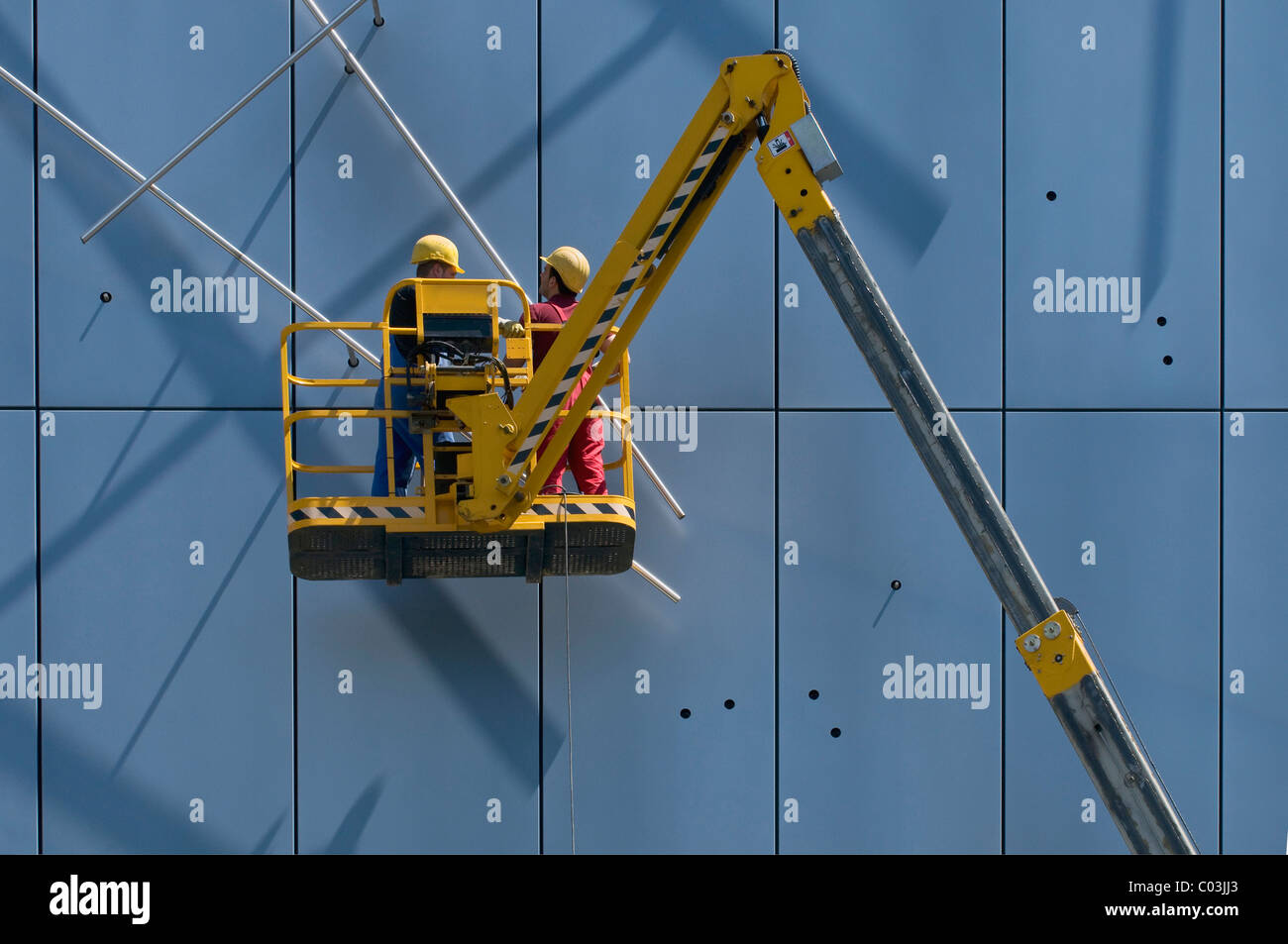 Travailleurs portant des casques de sécurité, debout sur une nacelle télescopique articulé et travaillant sur des éléments de façade Banque D'Images