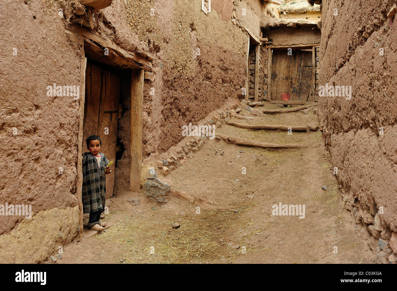 Petit garçon berbère debout devant une porte dans une ruelle étroite d'un adobe village, Kelaa M'gouna, Haut Atlas Banque D'Images