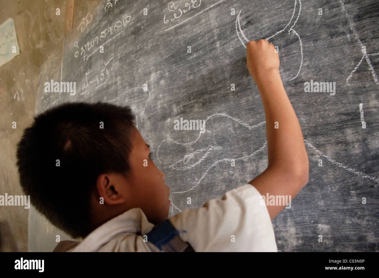 Un garçon étudiant est un dessin d'un animal sur un tableau, à un aperçu de l'école primaire en milieu rural au Laos communiste. Banque D'Images