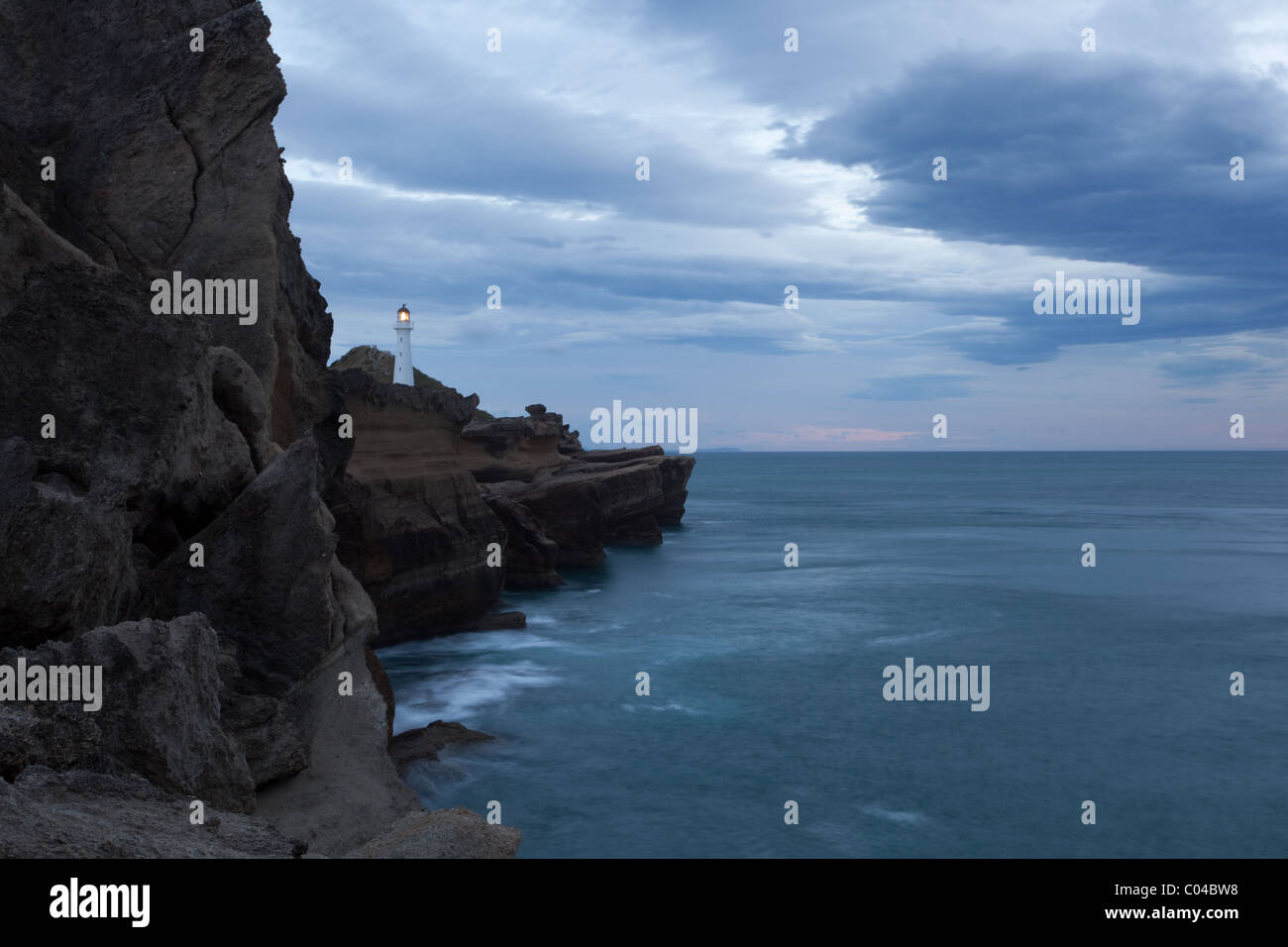 Delémont phare avec sa lampe sur, en Nouvelle-Zélande. La photographie a été prise à l'aube avec des nuages orageux en arrière-plan. Banque D'Images
