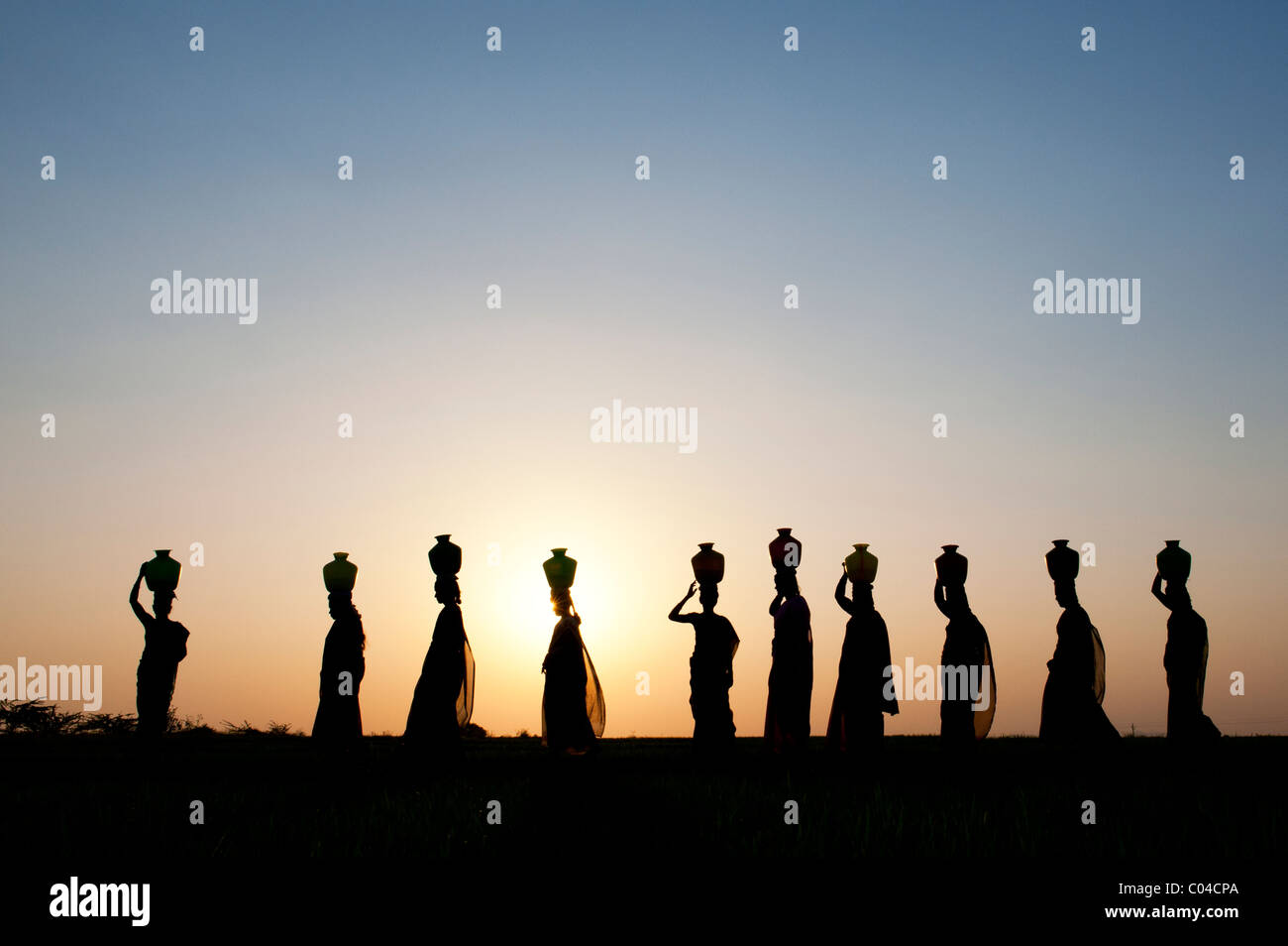 Groupe de femmes indiennes balade au coucher du soleil à transporter de l'eau sur leurs têtes des pots dans la campagne indienne. Silhouette Banque D'Images