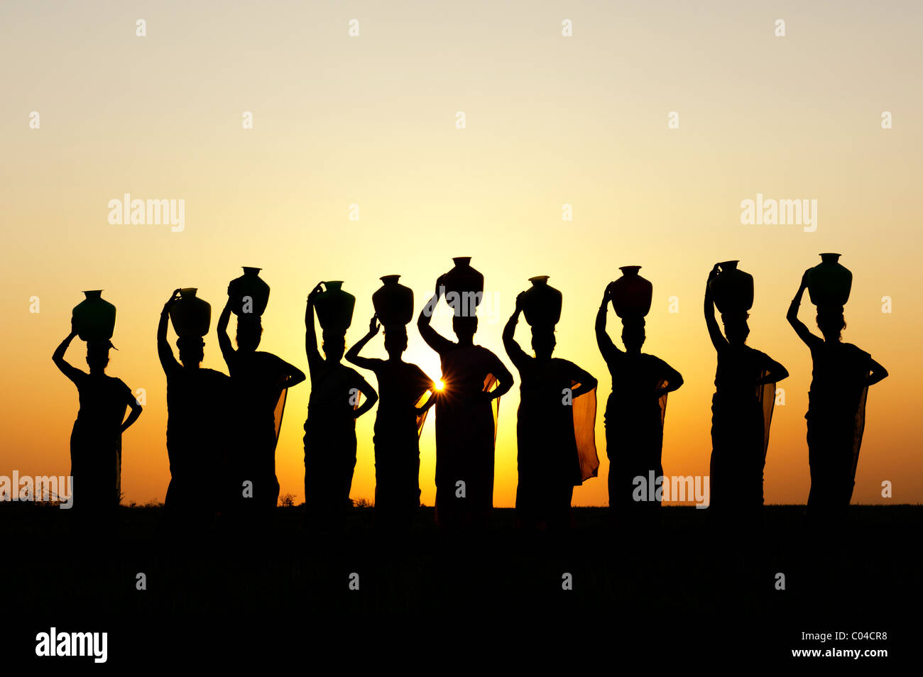 Groupe de femmes indiennes avec des pots d'eau permanent sur leurs têtes dans la campagne indienne. Silhouette Banque D'Images