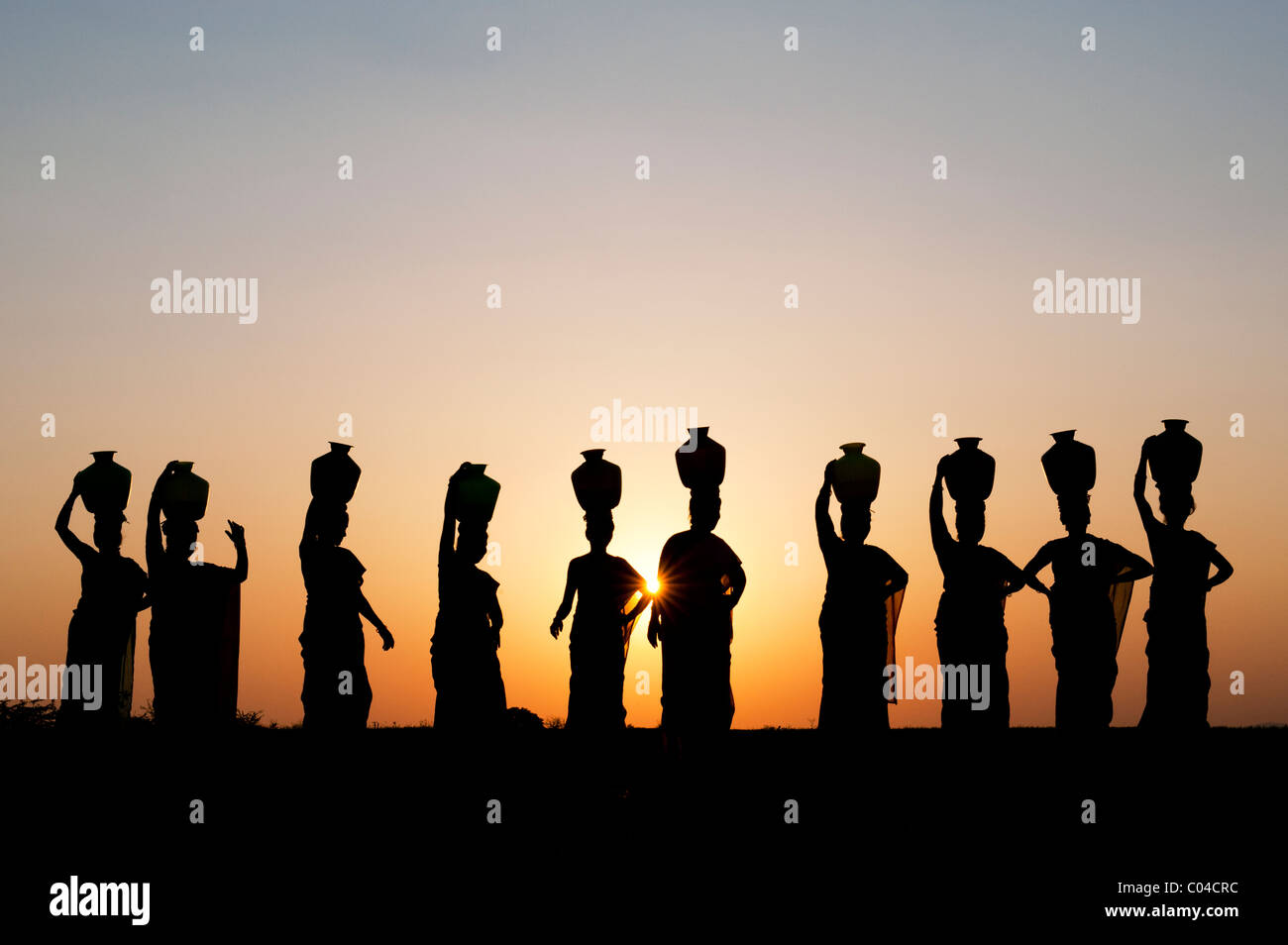 Groupe de femmes indiennes avec des pots d'eau permanent sur leurs têtes dans la campagne indienne. Silhouette Banque D'Images